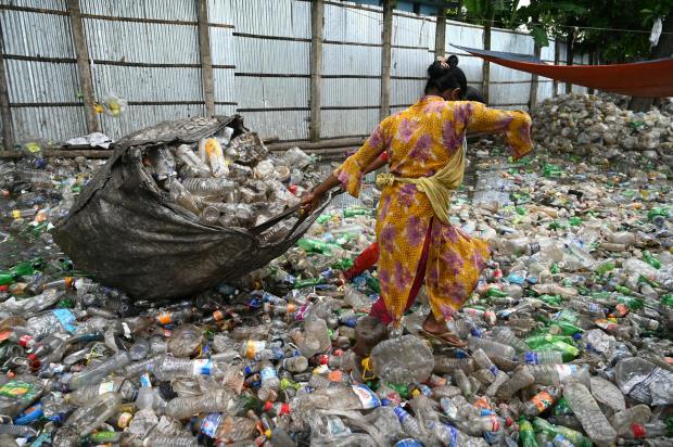 A worker at a recycling plant drags a sack full of discarded single-use plastic bottles.